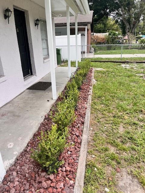 A concrete porch features a black door, exterior lighting, and a landscaped rock garden border — 8518 N LYNN AVENUE, TAMPA, FL