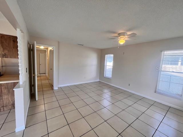 An empty room features light-colored tile flooring, beige walls, a ceiling fan, and two windows — 8518 N LYNN AVENUE, TAMPA, FL