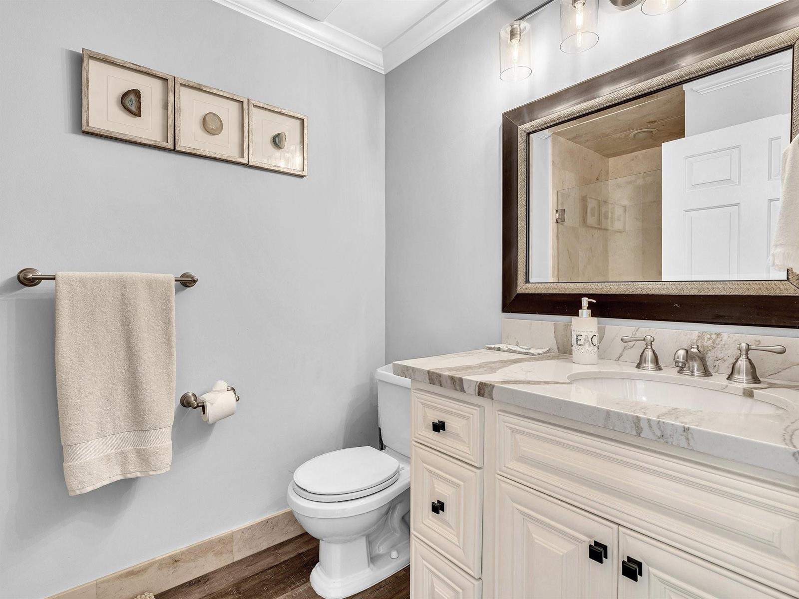 A bathroom features a white vanity with a marble countertop, a toilet, and framed wall art — 3602 S Ocean Boulevard # 102, Highland Beach FL 33487, HIGHLAND BEACH, FL