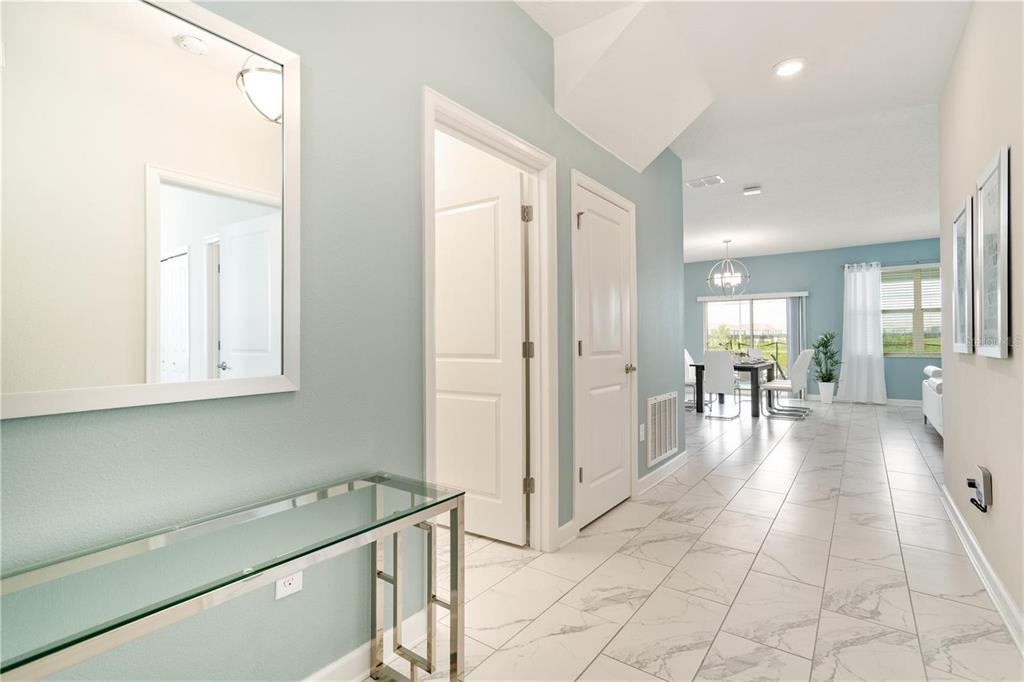 A bright hallway with light blue walls, white tile floors, and a glass console table — 1520 MAIDSTONE COURT, CHAMPIONS GATE, FL