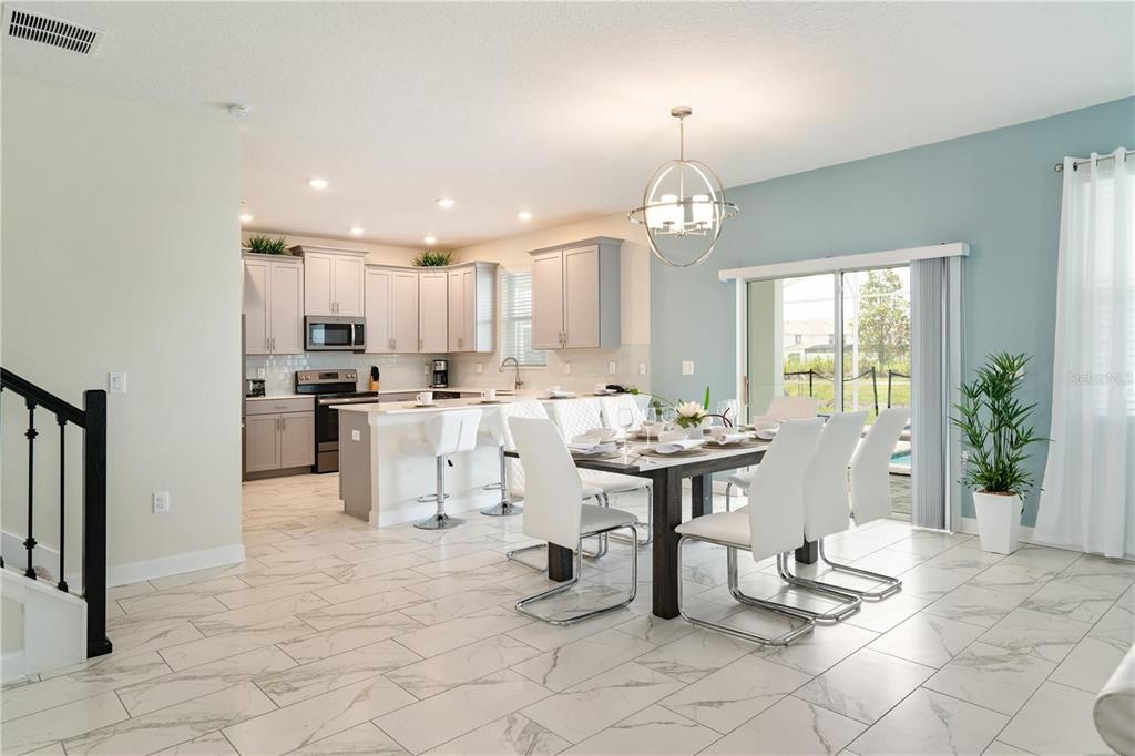 A dining area and kitchen with white cabinets, marble-look tile floors, and a sliding door — 1520 MAIDSTONE COURT, CHAMPIONS GATE, FL