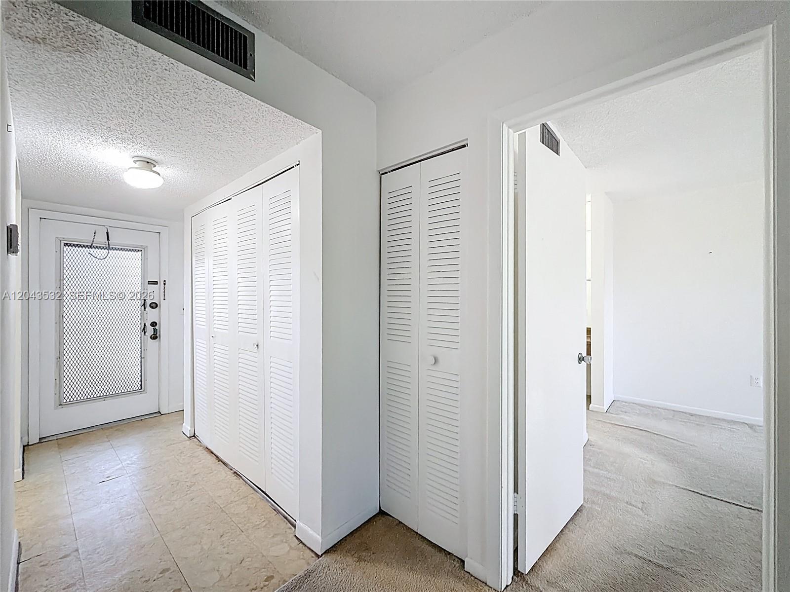 An entryway features a tiled floor, white louvered closet doors, and a doorway to a room — 6750 Royal Palm Blvd # 209E, Margate FL 33063, MARGATE, FL