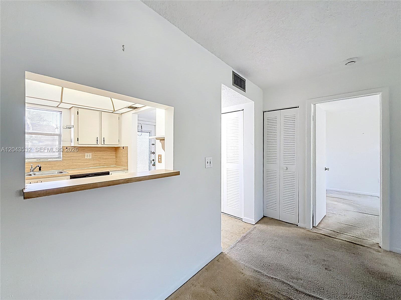 A view of a kitchen pass-through window, a hallway with closet doors, and a doorway — 6750 Royal Palm Blvd # 209E, Margate FL 33063, MARGATE, FL