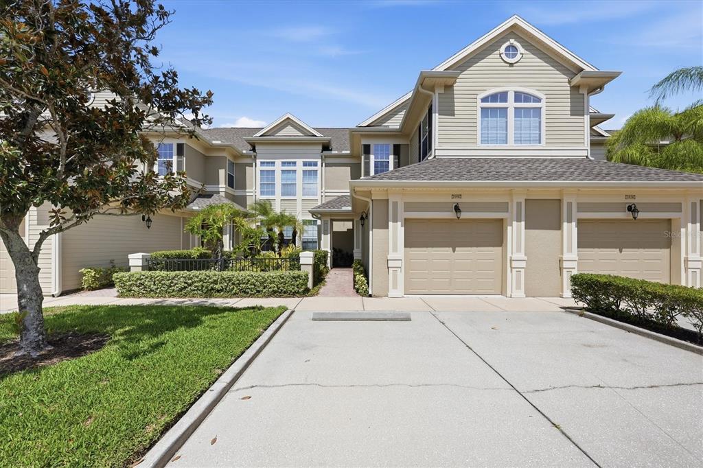 A two-story townhouse exterior with beige siding, two garage doors, and a landscaped front yard — 7930 TYBEE COURT UNIT 7930, UNIVERSITY PARK, FL