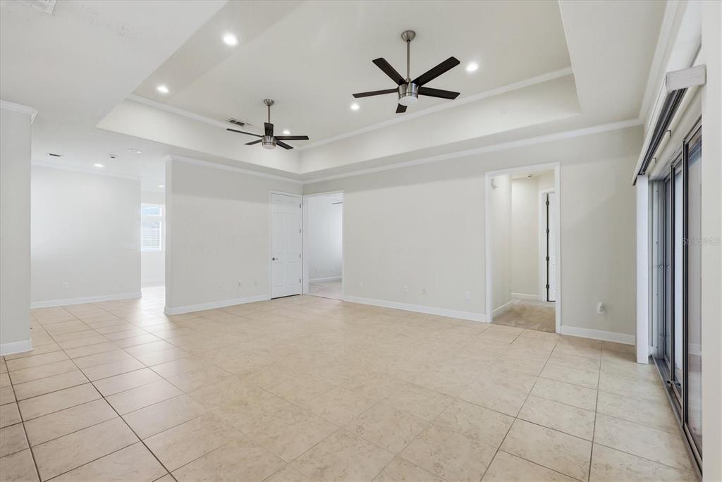 A spacious, empty room features light-colored tile flooring, a tray ceiling with two ceiling fans — 7930 TYBEE COURT UNIT 7930, UNIVERSITY PARK, FL