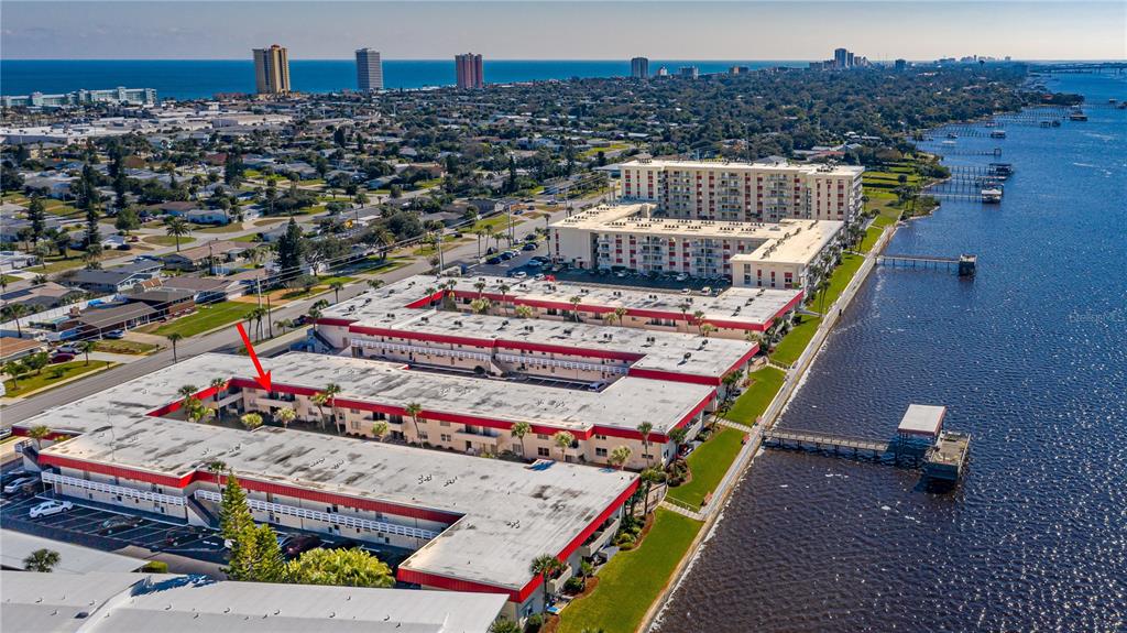 An aerial view shows a multi-story apartment complex with red trim situated along a river — 2901 N HALIFAX AVENUE UNIT 220, DAYTONA BEACH, FL