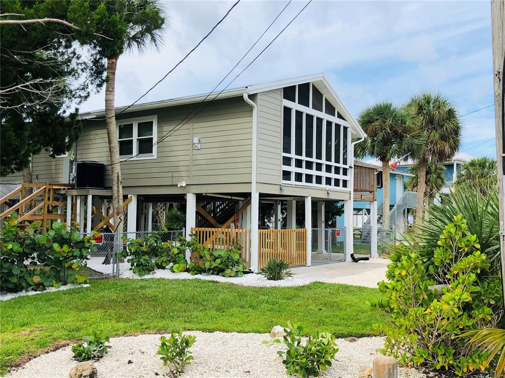A light green elevated house with a screened-in porch and a fenced-in ground level area — 3480 HARBOR DRIVE, WEEKI WACHEE, FL
