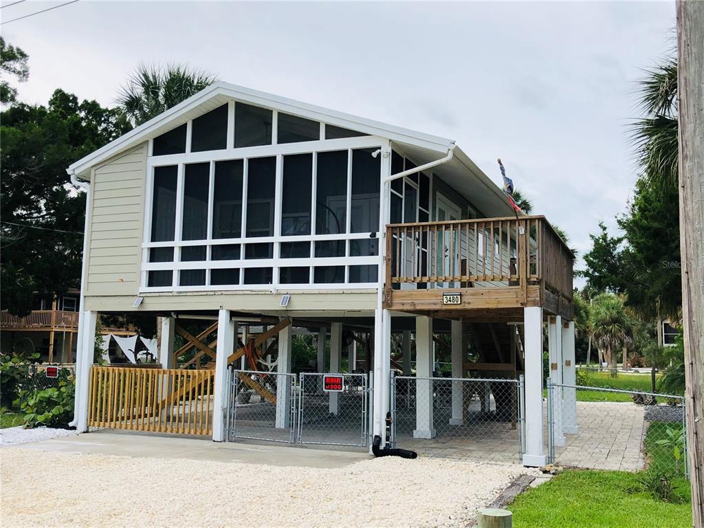 An elevated house with a screened-in porch, wooden deck, and a fenced-in ground level area — 3480 HARBOR DRIVE, WEEKI WACHEE, FL
