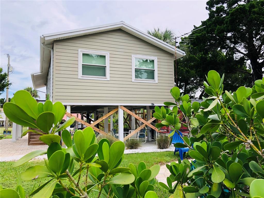 A two-story house with light green siding is elevated on wooden pilings above a patio — 3480 HARBOR DRIVE, WEEKI WACHEE, FL