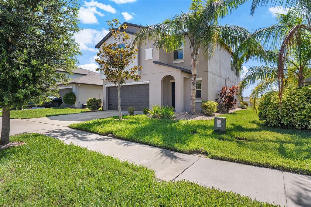 A two-story suburban house with a tan stucco exterior, a two-car garage, and palm trees — 3590 HANOVER DRIVE, NEW PORT RICHEY, FL
