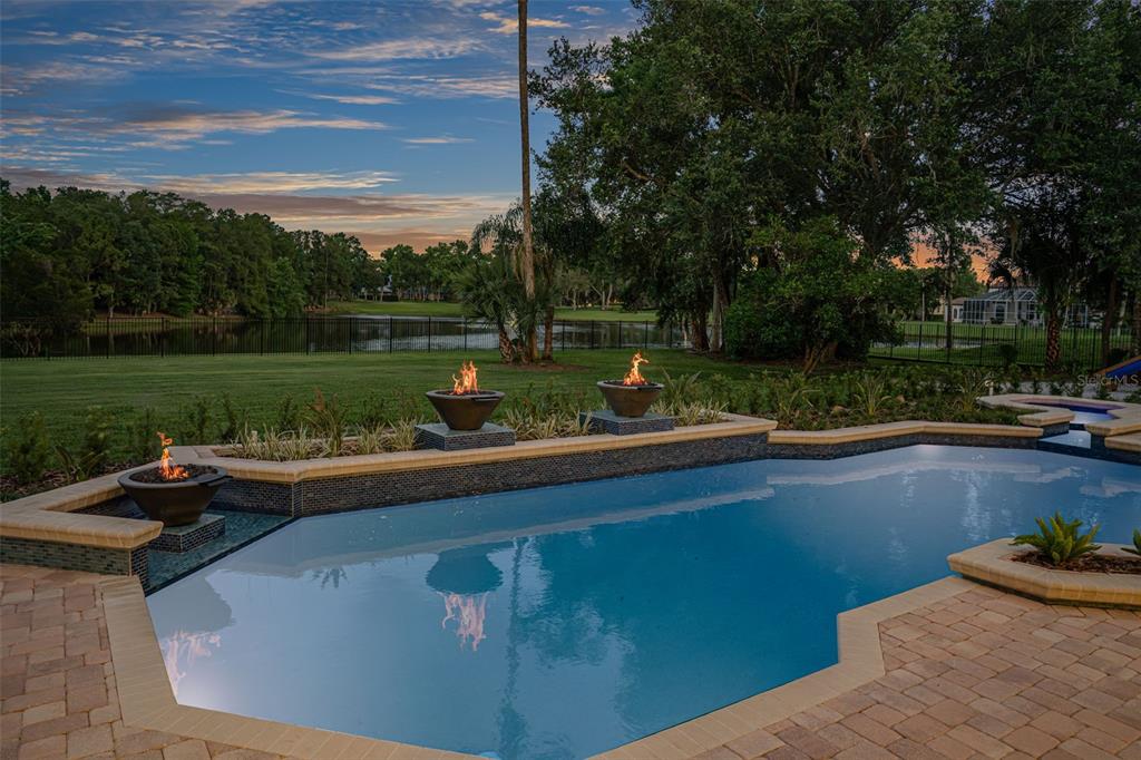 A swimming pool with fire bowls overlooks a grassy lawn and a lake at sunset — 3147 TALA LOOP, LONGWOOD, FL