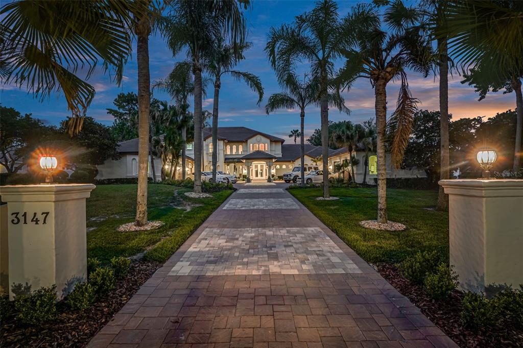 A paved driveway leads to a large two-story house surrounded by palm trees at dusk — 3147 TALA LOOP, LONGWOOD, FL