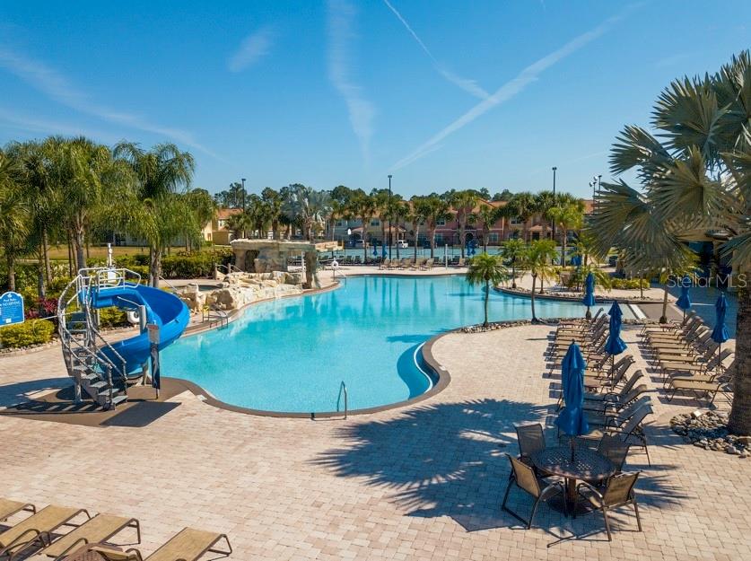 A resort-style swimming pool features a blue water slide, rock waterfall, and surrounding lounge chairs — 8945 CUBAN PALM ROAD, KISSIMMEE, FL
