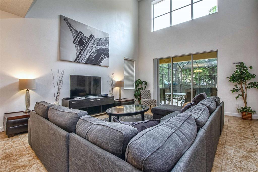 A living room features a large gray sectional sofa, a television, and high vaulted windows — 8945 CUBAN PALM ROAD, KISSIMMEE, FL