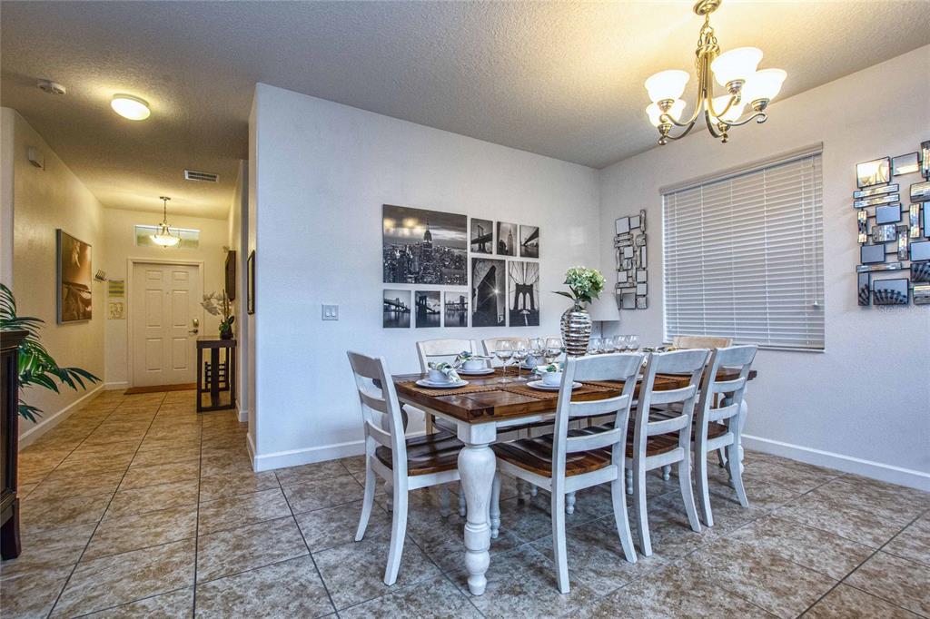 A dining room features a wooden table with white chairs, tile flooring, and wall art — 8945 CUBAN PALM ROAD, KISSIMMEE, FL