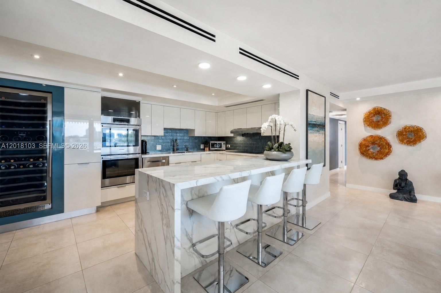 A modern kitchen features white cabinetry, a marble waterfall island, and four bar stools — 3 Grove Isle Dr # C410, Miami FL 33133, MIAMI, FL