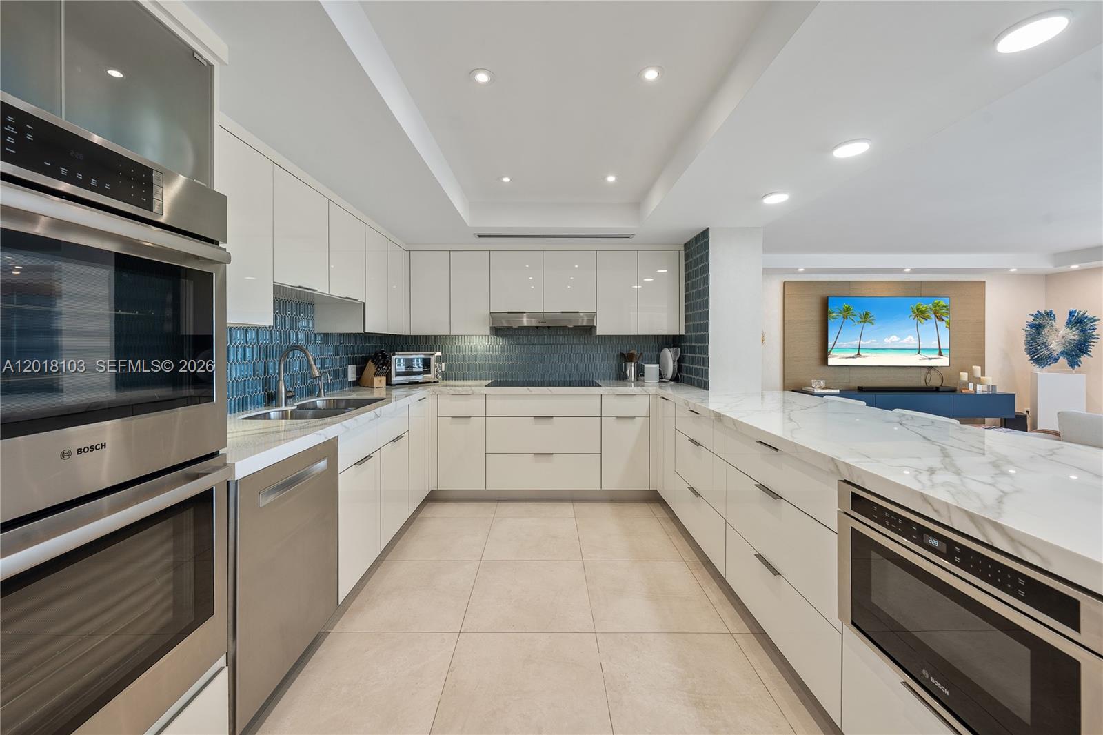A modern kitchen features white glossy cabinets, marble countertops, and a blue tiled backsplash — 3 Grove Isle Dr # C410, Miami FL 33133, MIAMI, FL