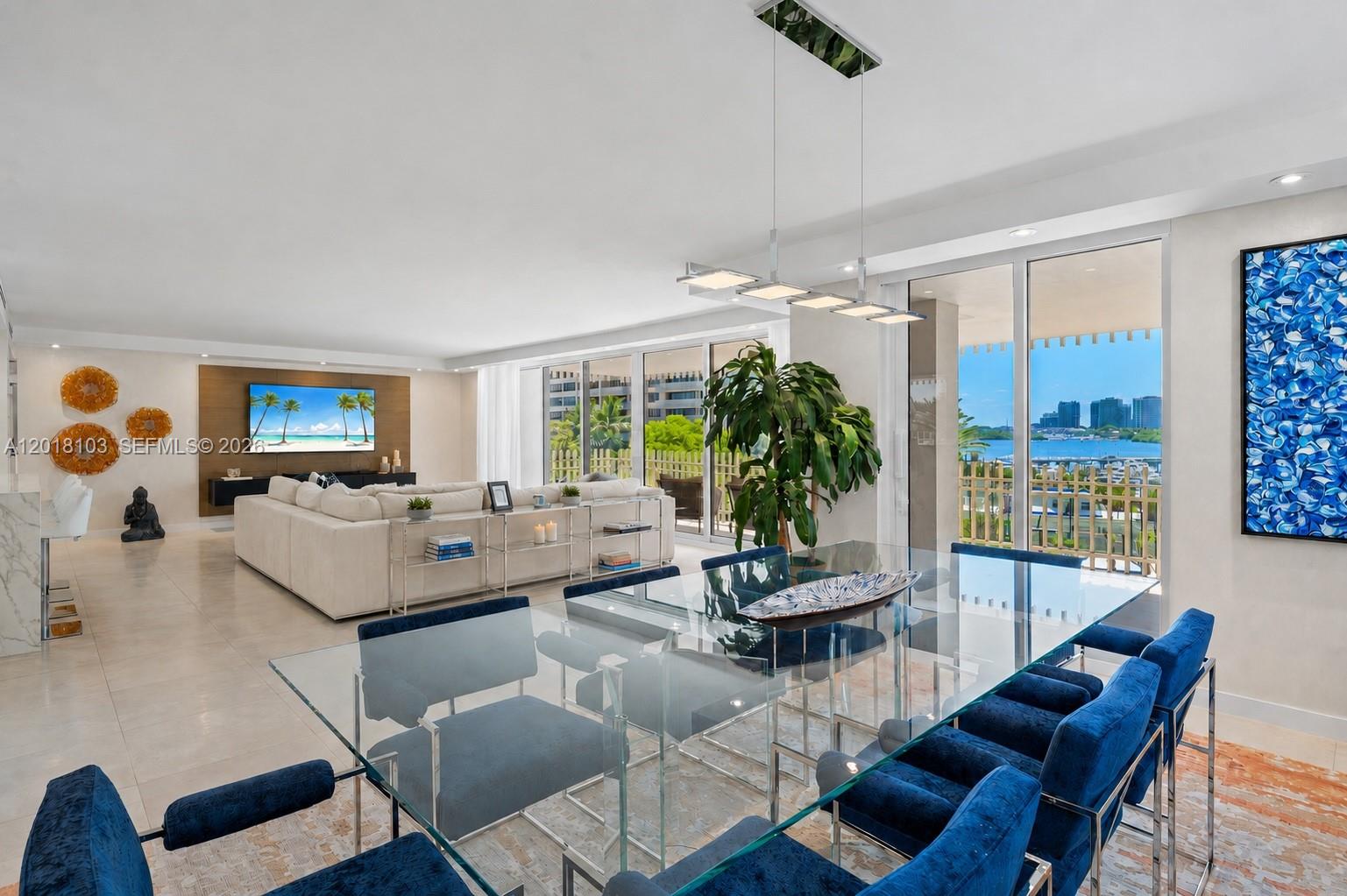 A modern dining and living area features a glass table, blue chairs, and balcony views — 3 Grove Isle Dr # C410, Miami FL 33133, MIAMI, FL