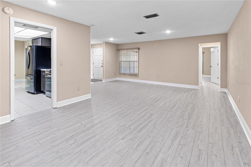 A spacious living area features light wood-look flooring, beige walls, and an adjacent kitchen — 1929 VALENCIA WAY, CLEARWATER, FL