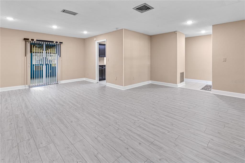 An empty room features light-colored wood-look flooring, beige walls, and a sliding glass door — 1929 VALENCIA WAY, CLEARWATER, FL