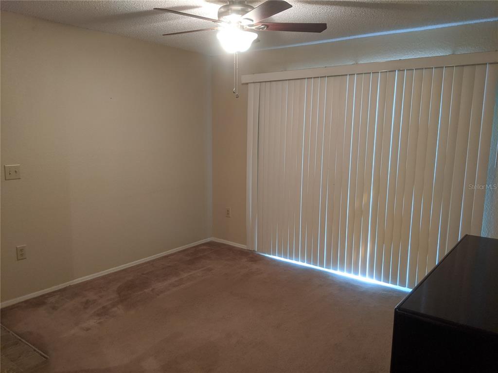 A bedroom features beige walls, brown carpeting, a ceiling fan, and vertical blinds over sliding doors — 3705 SW 27TH STREET UNIT 811, GAINESVILLE, FL