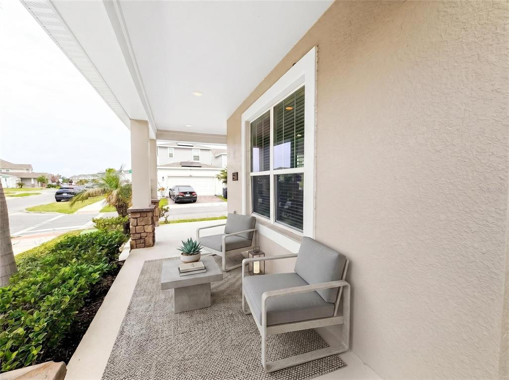 A covered front porch features two gray chairs, a small table, and a textured rug — 2401 VOLUNTEER AVENUE, KISSIMMEE, FL