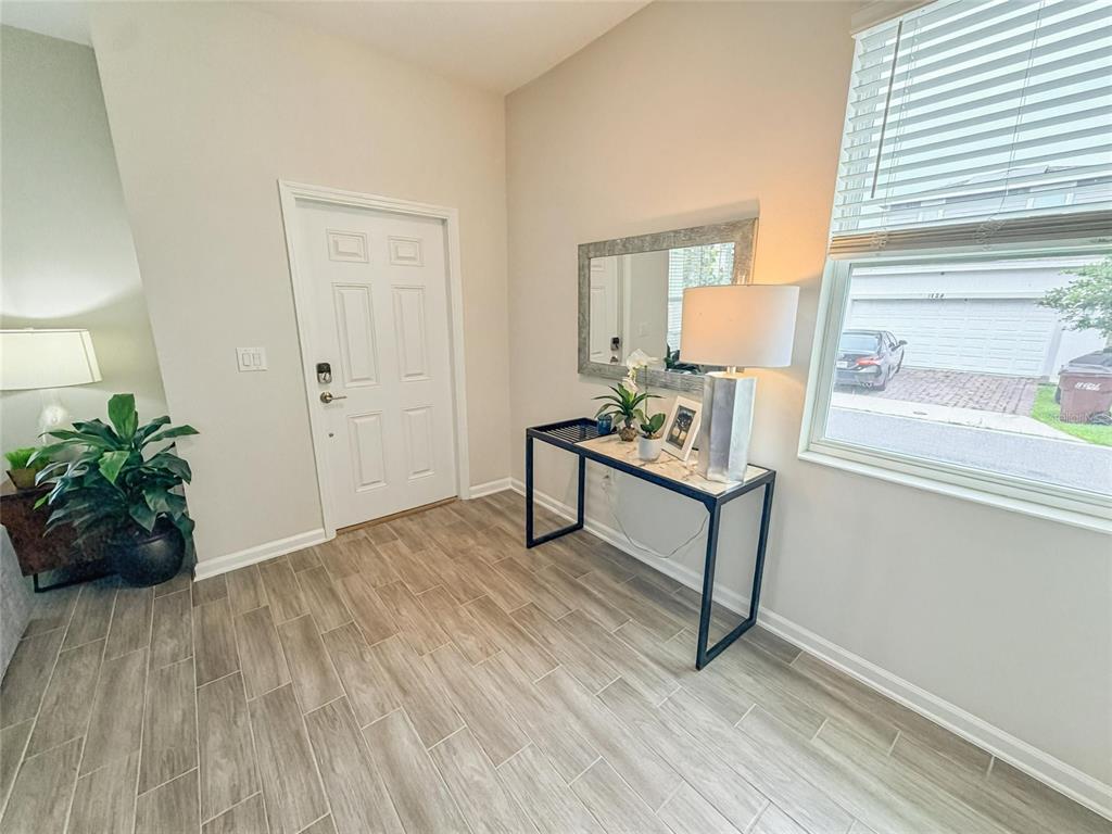 A bright entryway features wood-look tile flooring, a white front door, and a console table — 2401 VOLUNTEER AVENUE, KISSIMMEE, FL