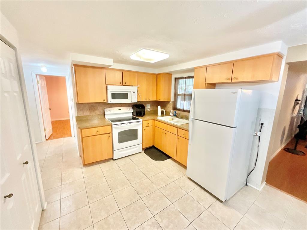 A kitchen features light wood cabinets, white appliances, tile flooring, and a window above the sink — 4750 GASLIGHT AVENUE, HOLIDAY, FL