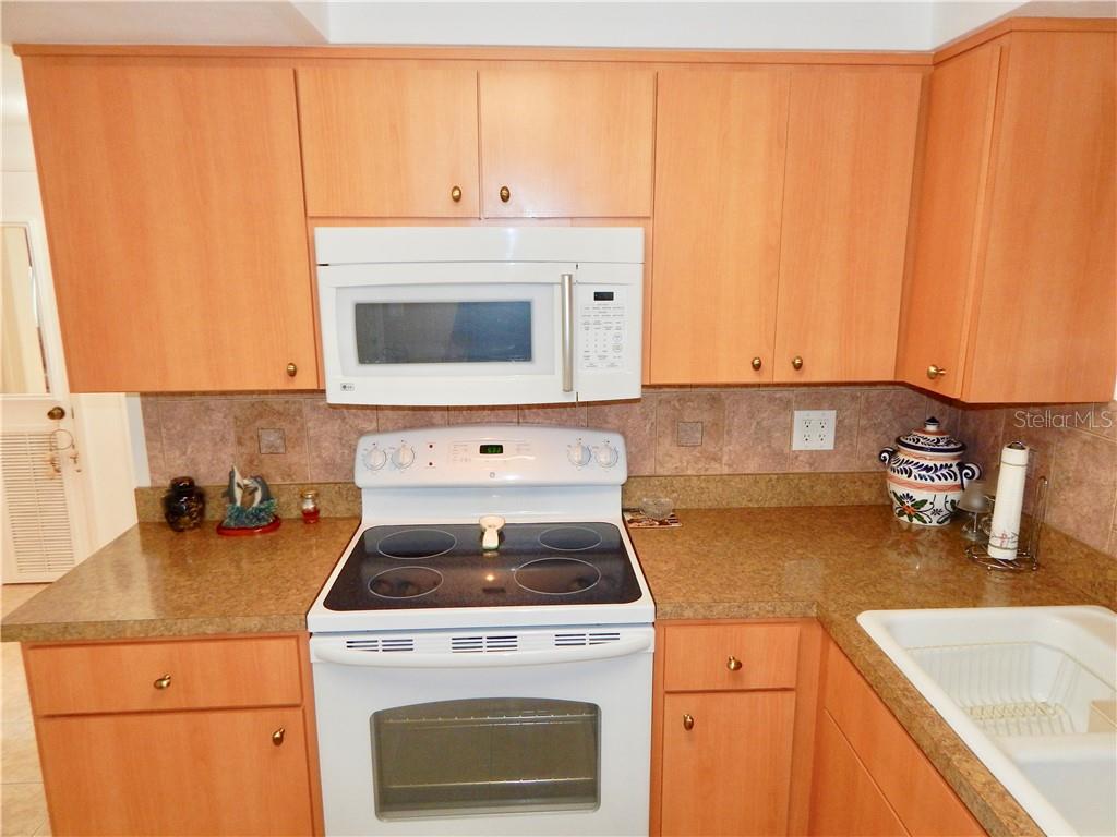 A kitchen features light wood cabinets, a white stove and microwave, and tan countertops — 4750 GASLIGHT AVENUE, HOLIDAY, FL