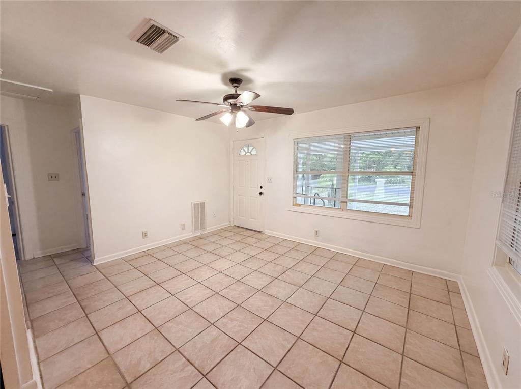 An empty room with beige tile flooring, a ceiling fan, and a white front door — 626 S 67TH STREET, TAMPA, FL