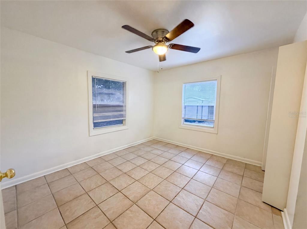 An empty room features beige tile flooring, white walls, two windows, and a ceiling fan — 626 S 67TH STREET, TAMPA, FL