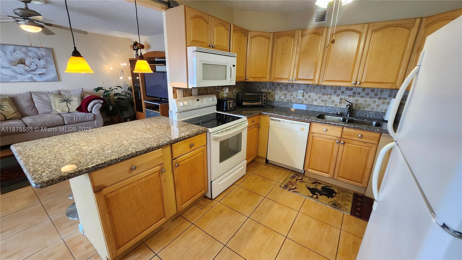 A kitchen with light wood cabinets, granite countertops, and white appliances opens to a living room — 3009 Ventnor G # 3009, Deerfield Beach FL 33442, DEERFIELD BEACH, FL