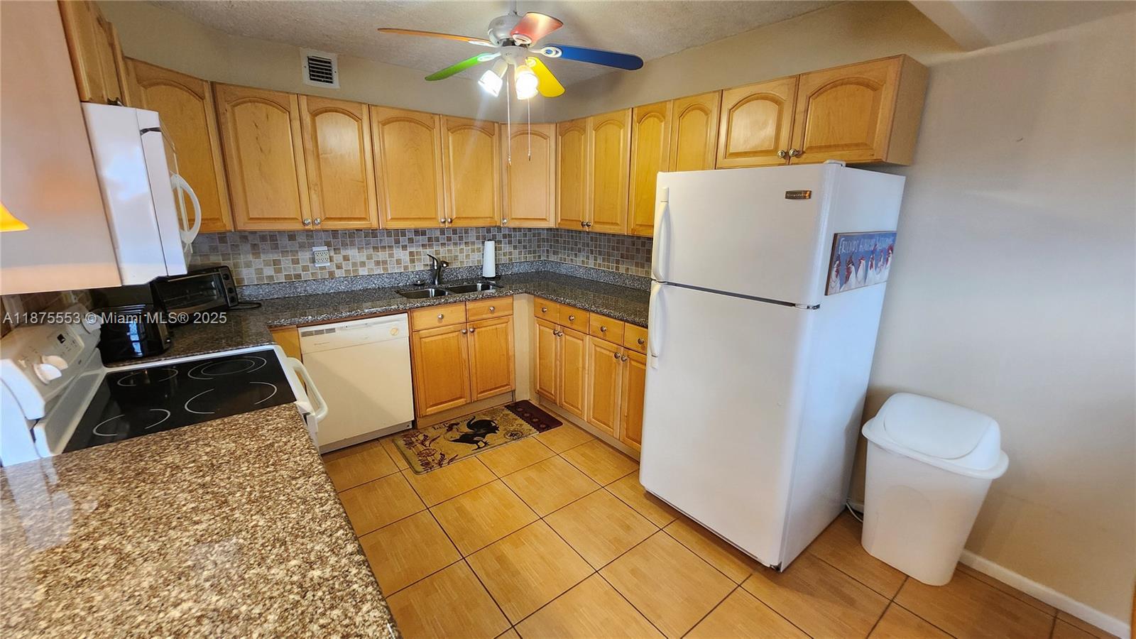 A kitchen features wood cabinets, granite countertops, white appliances, and a colorful ceiling fan — 3009 Ventnor G # 3009, Deerfield Beach FL 33442, DEERFIELD BEACH, FL