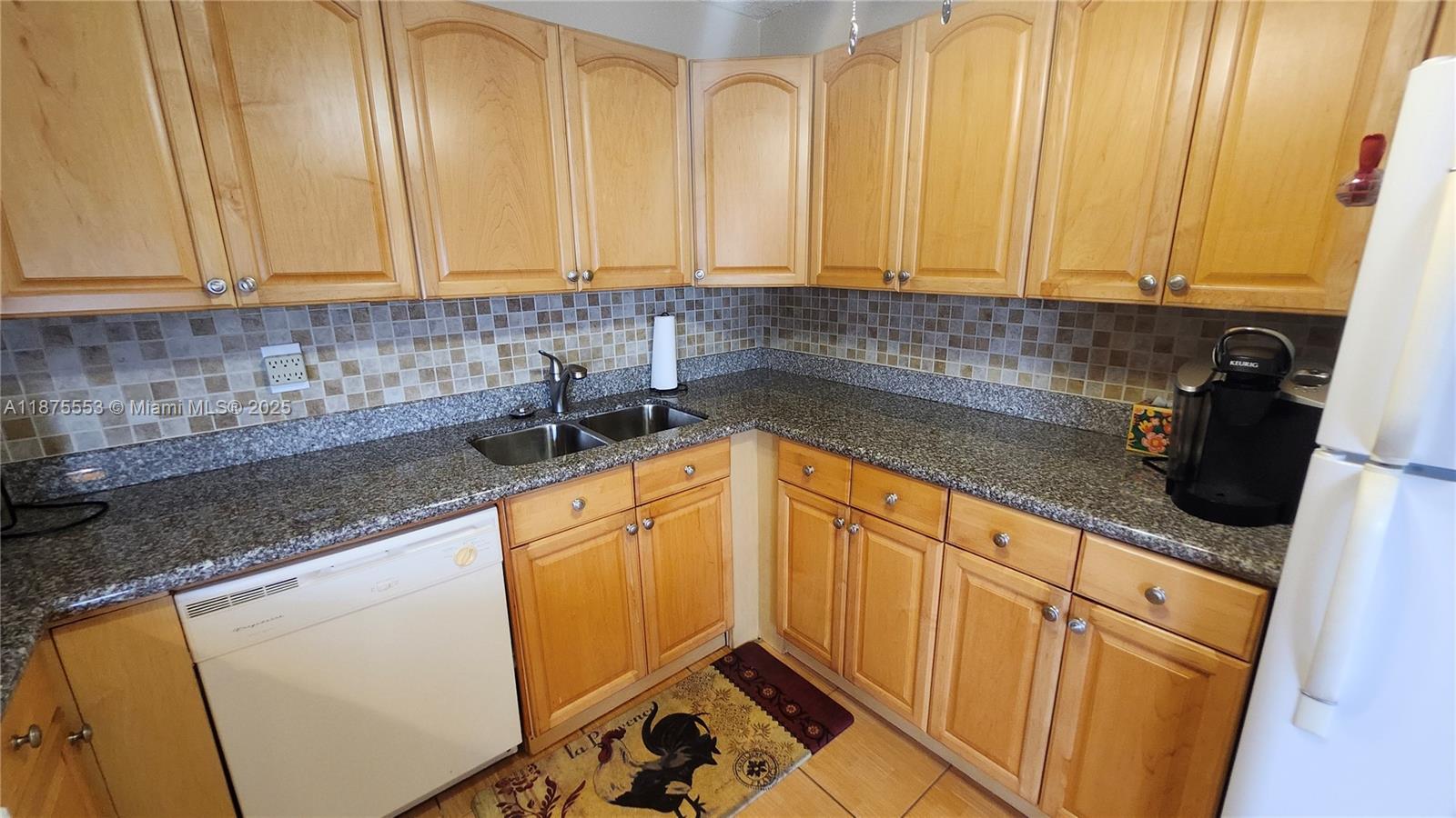 A kitchen features light wood cabinets, granite countertops, a tiled backsplash, and a white dishwasher — 3009 Ventnor G # 3009, Deerfield Beach FL 33442, DEERFIELD BEACH, FL