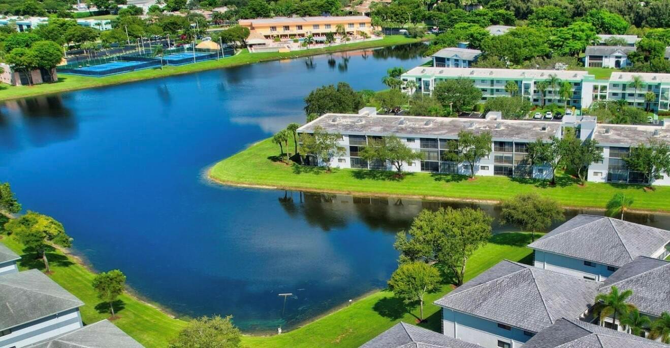 An aerial view shows apartment buildings situated around a large lake with tennis courts nearby — 15072 Ashland Place S # 117, Delray Beach FL 33484, DELRAY BEACH, FL
