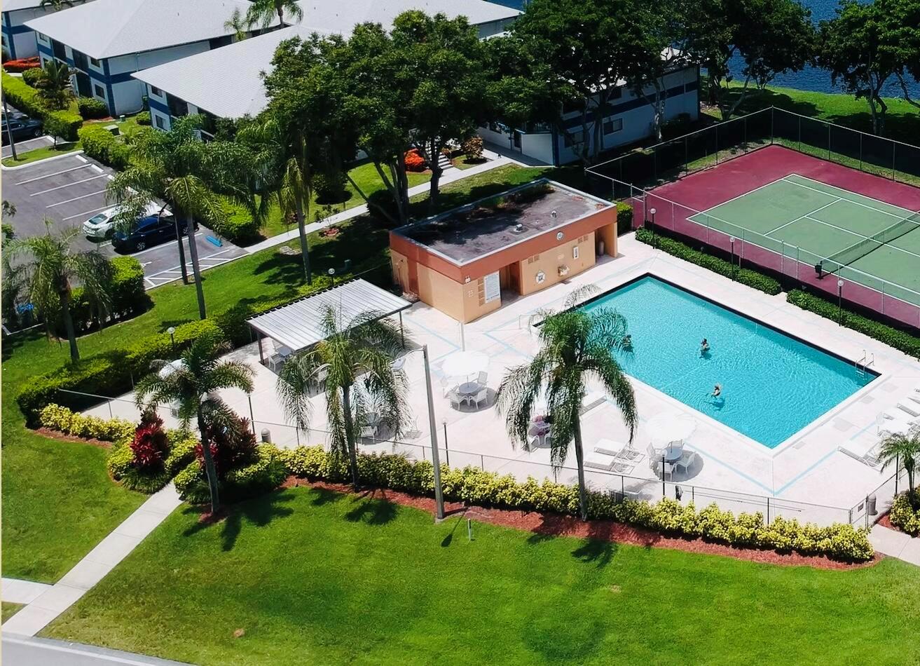 An aerial view of a swimming pool, tennis court, and parking area at an apartment complex — 15072 Ashland Place S # 117, Delray Beach FL 33484, DELRAY BEACH, FL