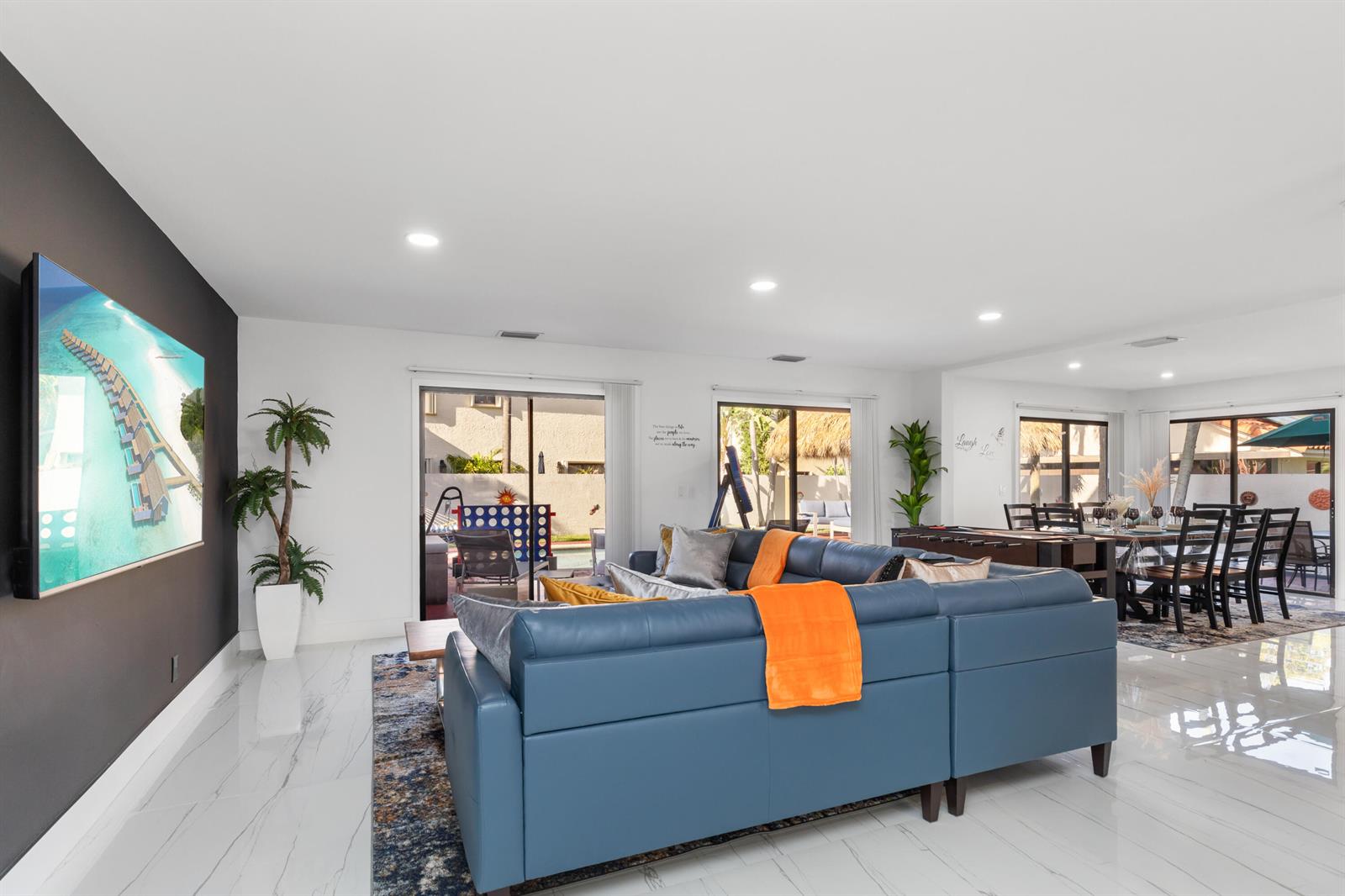 A living room with a blue sectional sofa, marble floors, and a large wall-mounted television — 484 NW 38th Terrace, Deerfield Beach FL 33442, DEERFIELD BEACH, FL