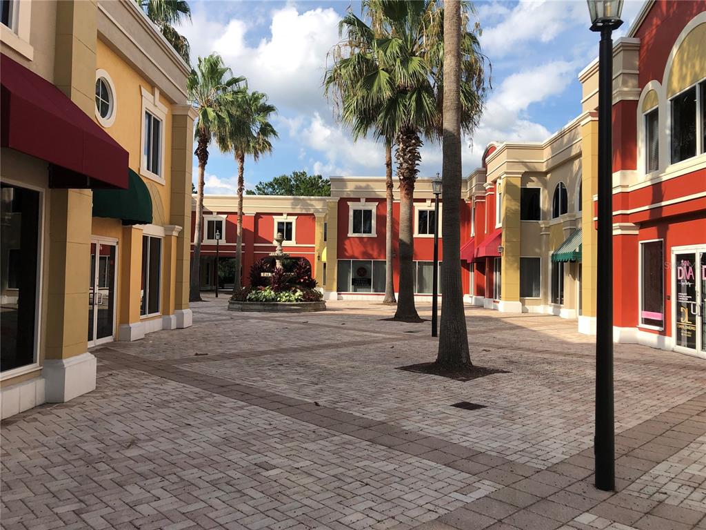 An outdoor courtyard features a central fountain, palm trees, and colorful commercial buildings with awnings — 2151 CONSULATE DRIVE UNIT 15, ORLANDO, FL