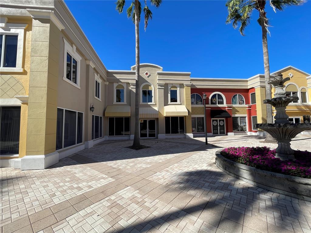 A paved courtyard features a stone fountain, palm trees, and multi-colored commercial building facades — 2151 CONSULATE DRIVE UNIT 15, ORLANDO, FL