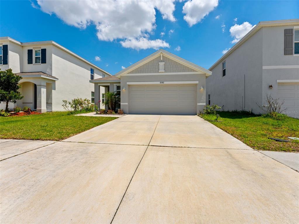 A single-story house with a two-car garage and a concrete driveway under a blue sky — 5782 HOLLINGWORTH TRAIL, WESLEY CHAPEL, FL