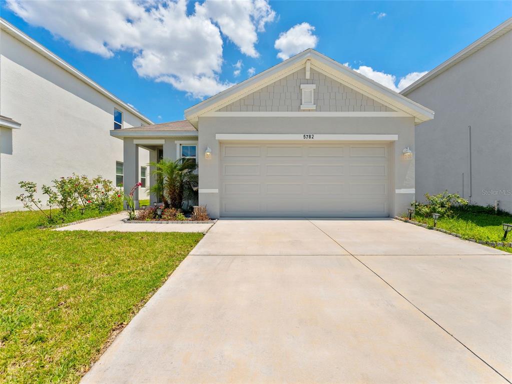A single-story house with a two-car garage, light gray siding, and a concrete driveway — 5782 HOLLINGWORTH TRAIL, WESLEY CHAPEL, FL