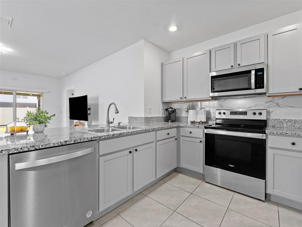 A kitchen features light gray cabinets, granite countertops, stainless steel appliances, and tile flooring — 5782 HOLLINGWORTH TRAIL, WESLEY CHAPEL, FL