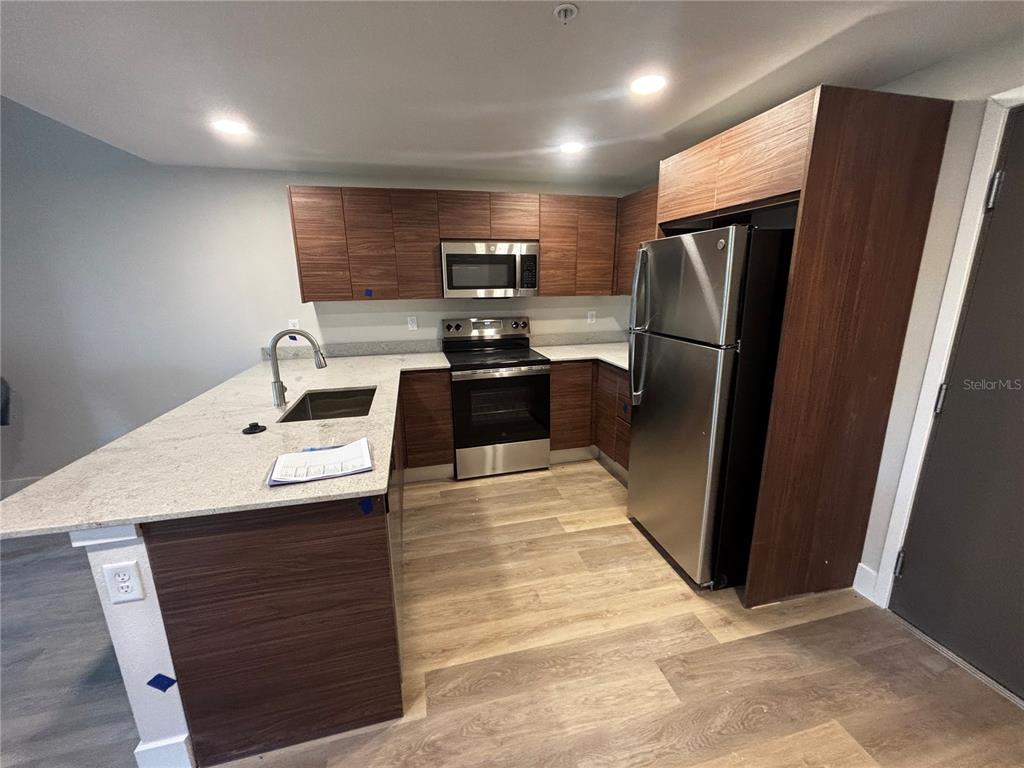 A kitchen features wood-grain cabinets, stainless steel appliances, and a light-colored granite countertop island — 4424 S TEXAS AVENUE UNIT 1-205, ORLANDO, FL