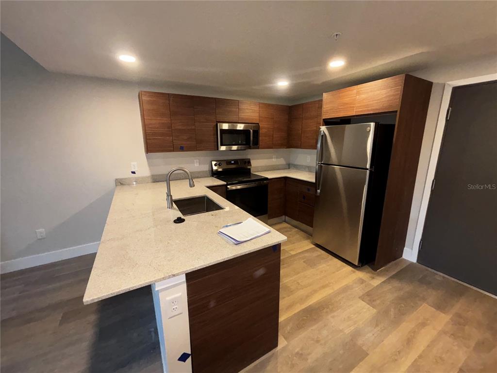 A modern kitchen features wood-grain cabinets, stainless steel appliances, and a light-colored stone island countertop — 4424 S TEXAS AVENUE UNIT 1-205, ORLANDO, FL
