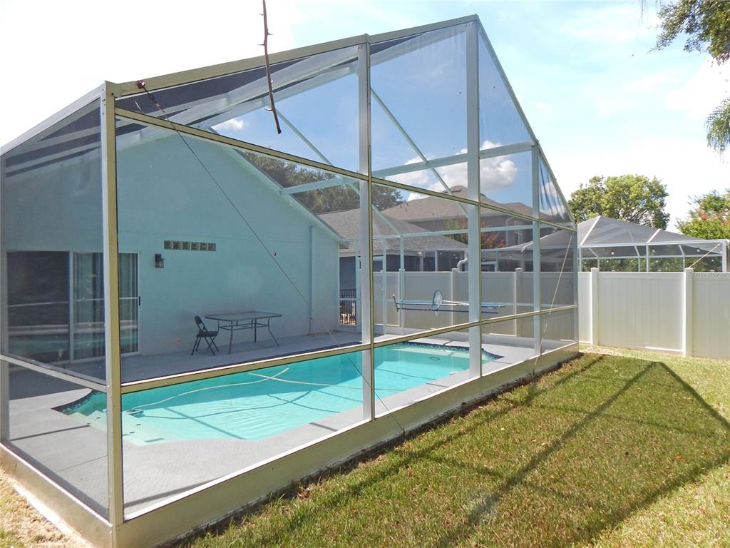 A swimming pool enclosed by a screened lanai structure in a backyard with a white fence — 5827 MEADOWPARK PLACE, LITHIA, FL