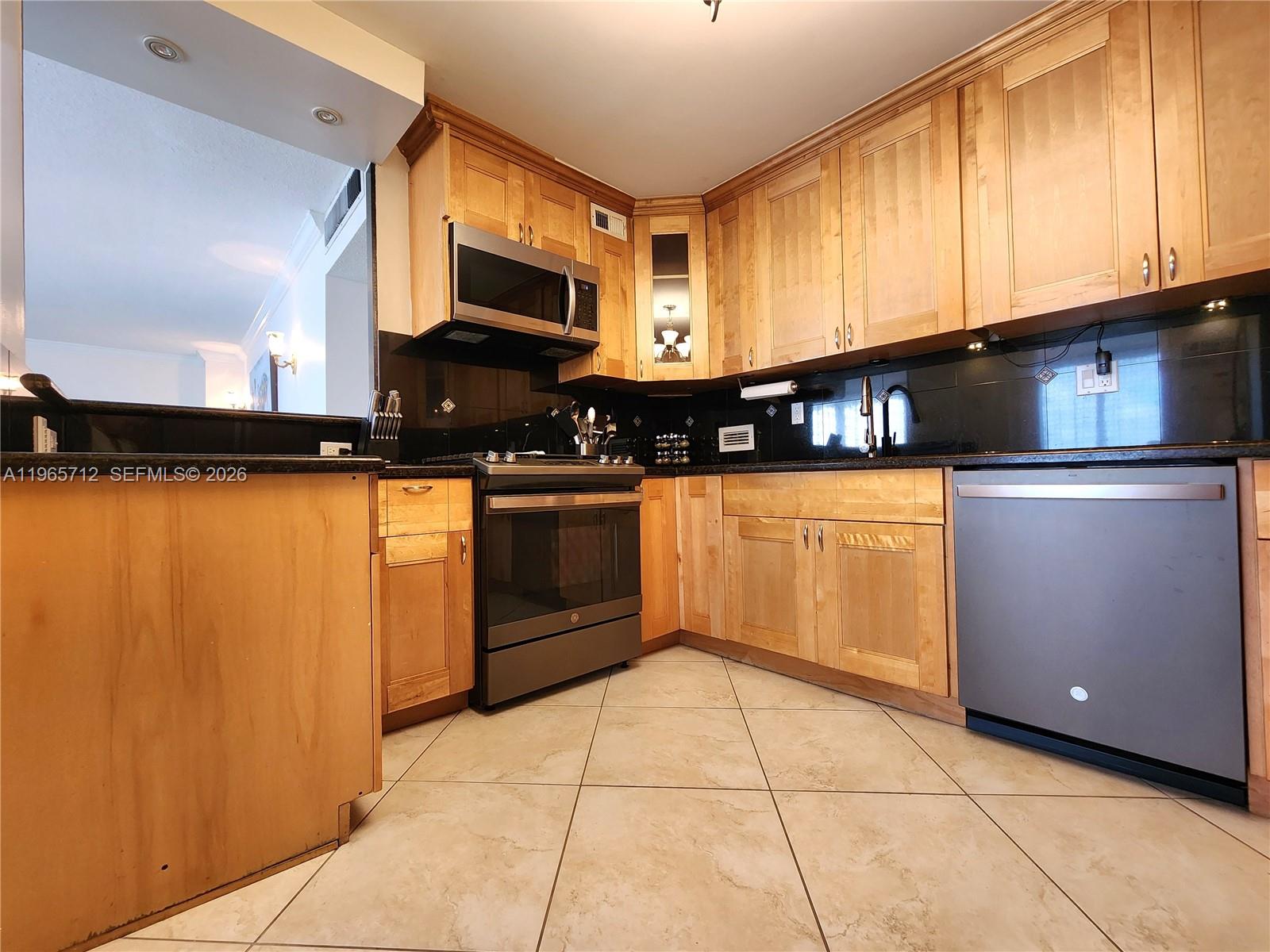 A kitchen features light wood cabinets, black countertops, stainless steel appliances, and beige tile flooring — 2030 S Ocean Dr # 626, Hallandale Beach FL 33009, HALLANDALE BEACH, FL