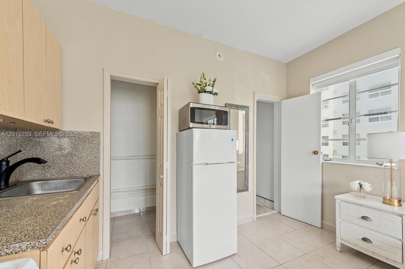 A small kitchen features light wood cabinets, granite countertops, a white refrigerator, and tiled floors — 301 86th St # 3A, Miami Beach FL 33141, MIAMI BEACH, FL