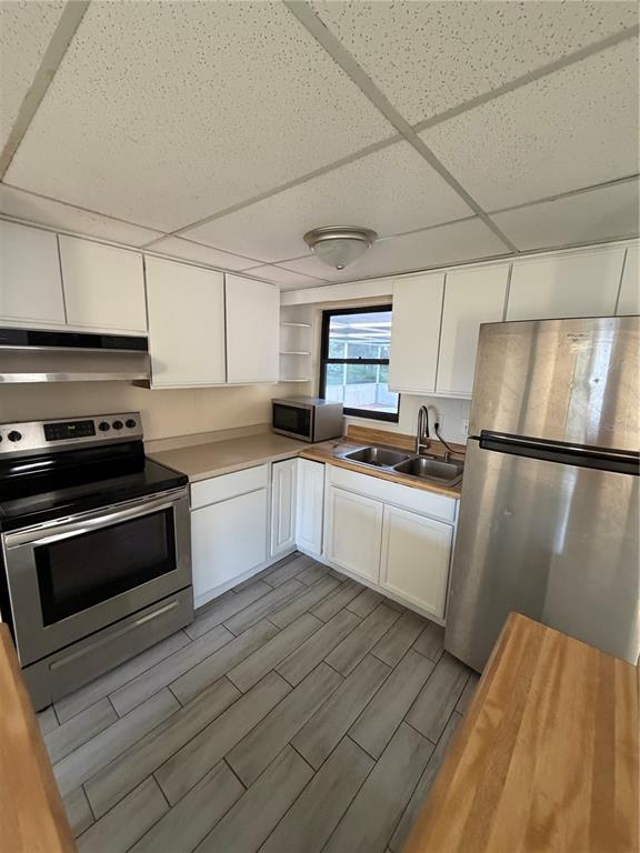 A kitchen features white cabinets, stainless steel appliances, a double sink, and gray tile flooring — 1923 FRUITLAND PARK CIRCLE, EAGLE LAKE, FL
