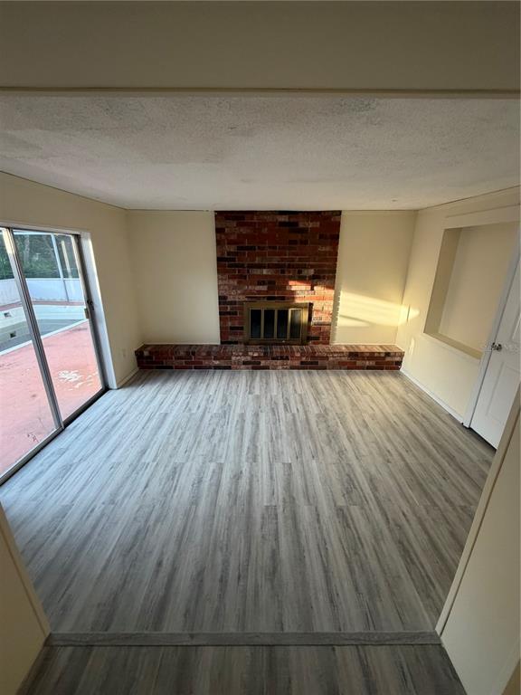 A living room features a brick fireplace, light wood-look flooring, and sliding glass patio doors — 1923 FRUITLAND PARK CIRCLE, EAGLE LAKE, FL