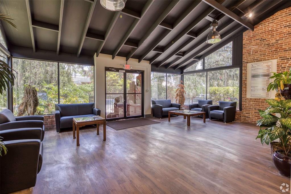 A waiting area with dark leather furniture, wood-look flooring, exposed ceiling beams, and brick walls — 7402 N 56TH ST STREET, TAMPA, FL